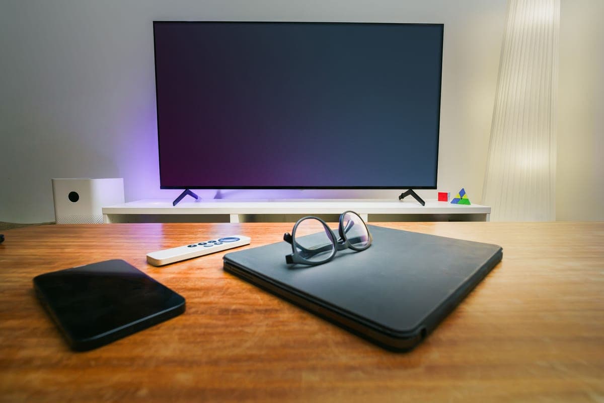 A compact smart home hub on a bookshelf beside a plant in a bright living room.